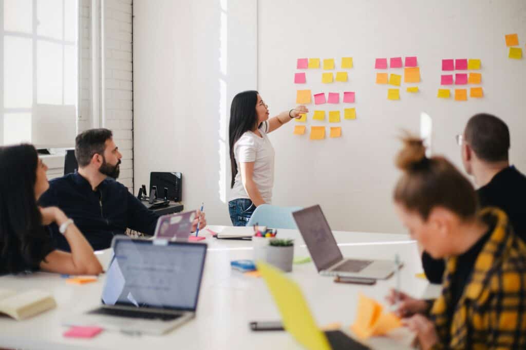 A meeting and a women is positioning post-it notes on a whiteboard.